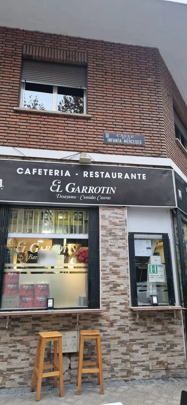 Fachada de la esquina con el rótulo de El Garrotín, dos taburetes y la placa de la calle Infanta Mercedes