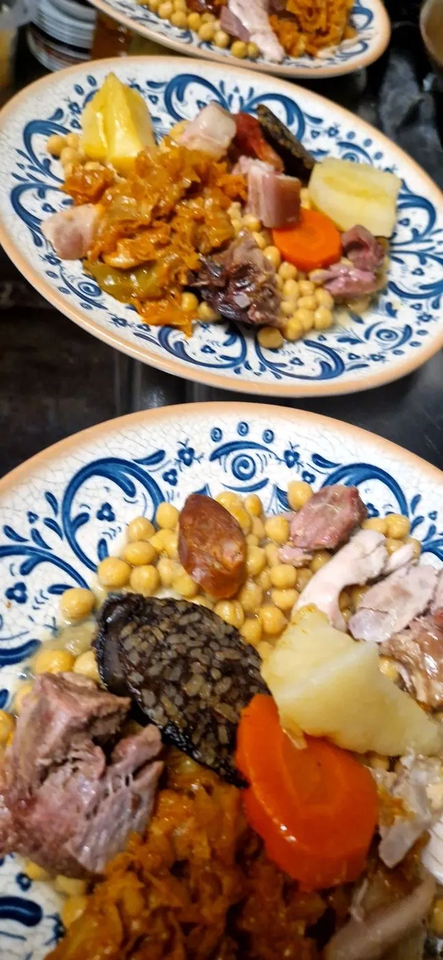Dos platos de cocido con garbanzos, chorizo, morcilla, carne, patata, zanahoria y repollo