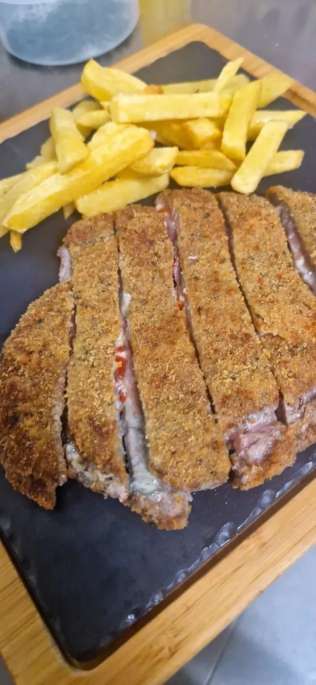 Cachopo cortado en tiras sobre una pizarra, con patatas fritas