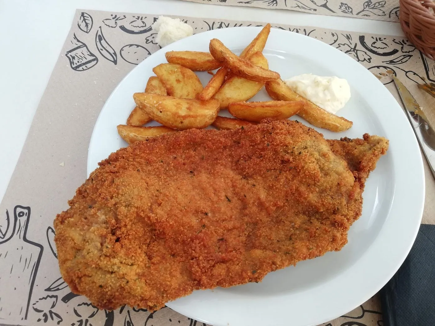 Escalope empanado con patatas gajo y salsa en un plato blanco