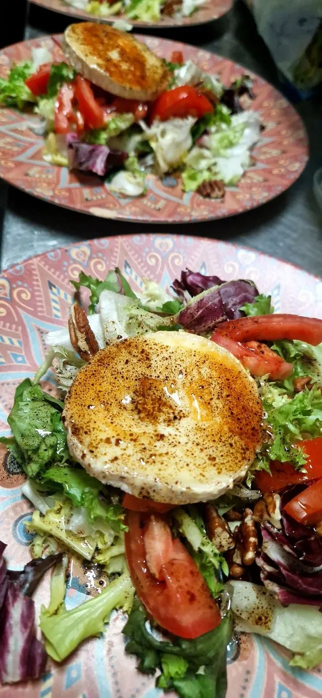 Ensalada con queso de cabra templado, tomate, nueces y lechugas en un plato rosa